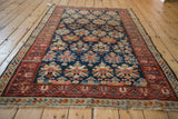 Vintage Caucasian rug detail: even wear visible on red geometric borders and navy field with floral palmettes.