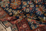Folded vintage Caucasian rug detail: navy field with floral palmettes, aubergine geometric border.