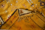 Saffron yellow vintage Moroccan rug folded corner showing shaggy pile, dark selvage, and striped foundation.