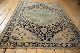 Distressed Malayer rug edge showing ornate navy, ivory, and blush border motifs.