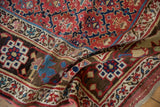 Textured close-up of antique Kurdish rug with red, blue, and dark brown tribal patterns.