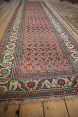 Long perspective view of a vintage Hamadan runner's repeating boteh pattern on a chestnut red field.