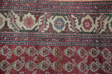 Hand-knotted boteh motifs on a chestnut red field next to the detailed floral ivory border.