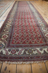 Long angled view of a vintage Hamadan runner with a repeating red boteh pattern and ivory borders.