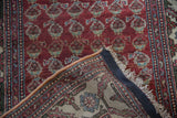 Folded corner of a vintage Hamadan rug reveals its hand-knotted back and red boteh pile.