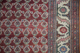Hand-knotted boteh pattern in red and blue against the vintage rug's detailed ivory floral border.