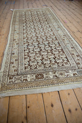 Angled view of distressed Kurdish Hamadan runner, beige plant motifs on brown field.