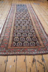 Angled perspective of an antique Kurdish runner with a staggered boteh pattern and intricate borders.
