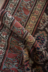 A rolled view of a collector's antique Kurdish rug highlighting the supple texture and boteh border.