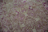 Close-up of a distressed vintage rug's pile, showing magenta and silver blossom motifs worn to the knot heads.