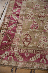 Angled view of a distressed Karabagh rug's textured pile and raspberry red serrated leaf border.