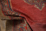 A folded corner of a vintage Serab rug showing the textured camel hair border and abrashed red pile.