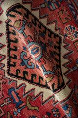 Hand-knotted pile texture on a rolled vintage Heriz rug, revealing geometric patterns in red, blue, and gold.