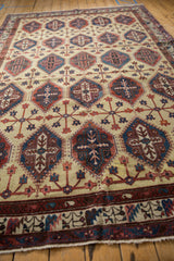 Vintage Persian carpet from an angle, showing the repeating panel design in red, blue, and cream.