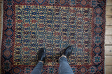 Looking down at the saffron, navy, and madder red floral lattice of an antique Afshar rug.
