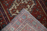 Vintage Karaja rug corner folded back, displaying fine woven foundation and red, blue, ivory geometric patterns.