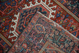 Vintage Karaja rug corner showing cherry red, navy geometric patterns, and tattered side selvage.