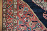 Malayer rug's main border featuring geometric vine, madder red field, and navy animal motifs.