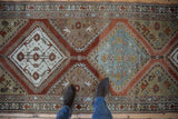 A distressed Malayer runner with interconnected diamond medallions in rust, slate blue, and sand tones.