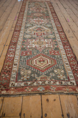 Geometric motifs and pinwheel flowers on dusty teal field with chestnut red border.