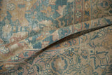 Folded distressed Agra carpet showing dusty ocean blue palmettes and textured wear with visible foundation.