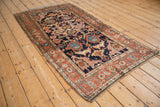Angled view of an antique Kurdish rug highlighting its palmette designs and rich terracotta border.