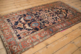 Angled view of an antique Kurdish rug with dragon-inspired floral elements and a terra cotta border.
