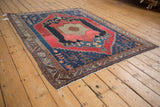 Fringed end of an antique Malayer rug, showing primitive navy, cherry red, and beige patterns with even wear.
