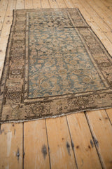 Faded teal and beige distressed Malayer rug corner, highlighting worn pile and tattered edge detail.