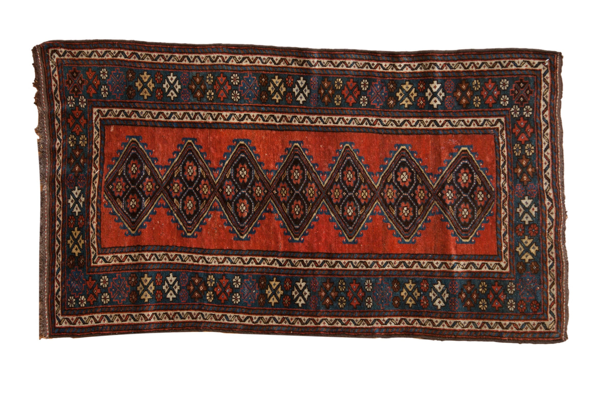Antique Kurdish rug with interconnected diamond medallions on a madder red field framed by a cobalt blue border.