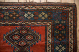 Corner of an antique Kurdish rug showing a geometric blossom border in cobalt blue and madder rust.