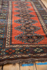 Angled view of an antique Kurdish rug's repeating diamond medallions and richly textured low pile.