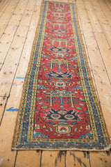 Vintage Heriz runner close-up showing tattered end, cherry red field, and blue-gold geometric borders.