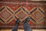 Hamadan rug detail with stepped medallions, pictorial figures, brick red and gold tones.