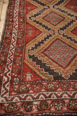 Vintage Hamadan rug close-up showing brick red field, stepped diamond motifs, and tribal figures.