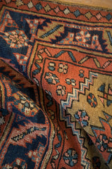 Angled detail of the hand-knotted pile and pearl seed border on an antique Persian Heriz rug.