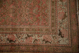 The corner spandrel of a distressed Malayer rug with a faded Herati design in blush, brown, and beige.