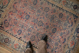 Distressed antique Malayer rug close-up, faded blush red and navy geometric patterns.
