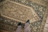 On-floor view of the antique Malayer rug's worn texture and floral pattern in ivory and navy blue.