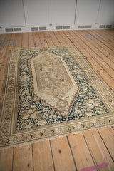 Angled view of an antique distressed Malayer rug showing its elongated ivory medallion and navy field.