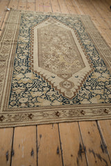 Angled view highlighting the elongated medallion and borders of a distressed antique Malayer rug.
