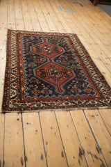 Antique Persian Afshar rug with red double medallions on a navy blue field, viewed from an angle.