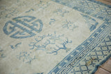 Close-up on the distressed ivory wool of a Peking rug with blue pearl and trellis borders.