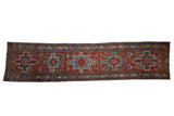 Vintage Persian Heriz rug runner, repeating geometric medallions, cherry red field, blue and gold motifs.