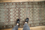 Distressed vintage Caucasian runner featuring repeating diamond lattice motifs, muted brown and ivory tones.