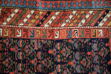 Kurdish rug's reciprocating pawn design border and navy field with henna plant motifs.