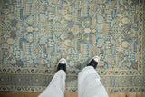 A person's perspective of a distressed Tabriz rug, highlighting its soft blue and beige geometric pattern.