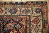 Corner of an antique Qashqai carpet showing even wear, pinwheel florals, and a multi-colored barber pole border.