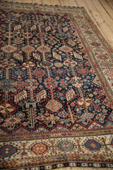 Low-pile texture and dense tribal motifs of an antique Qashqai carpet shown from an angled perspective.
