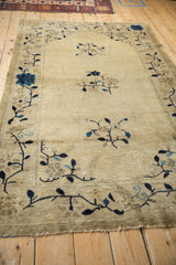 Fringed end of an antique Chinese Peking rug with navy blue floral vines on a beige field.